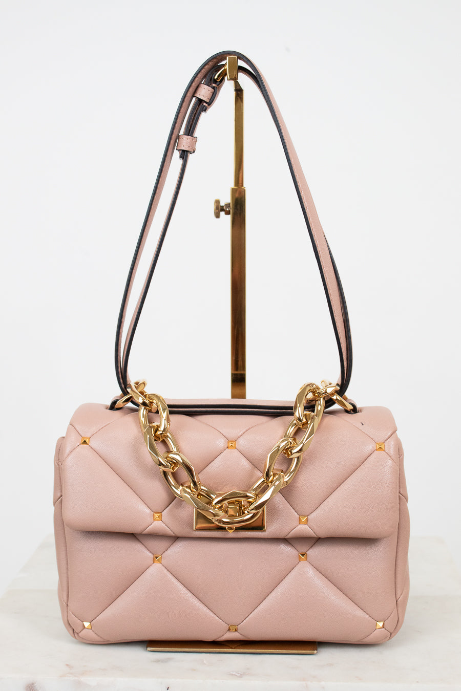 Pink quilted handbag with gold chain detail on a white background