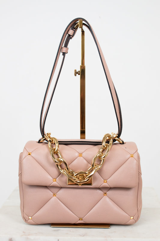 Pink quilted handbag with gold chain detail on a white background