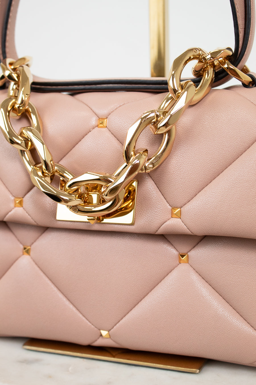 Pink handbag with gold chain detail on a light background