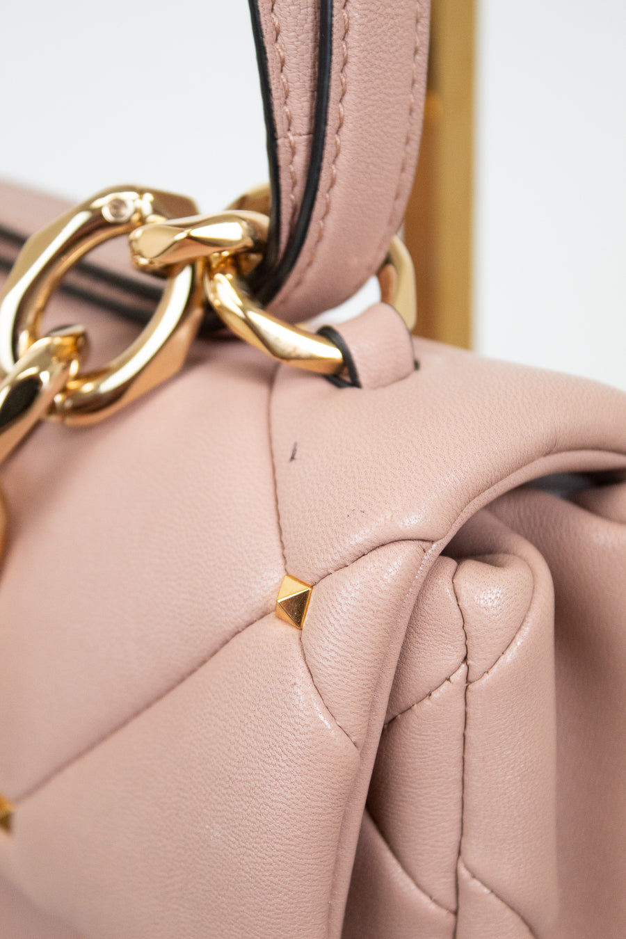 Close-up of a pink handbag with a gold chain detail on a light gray background