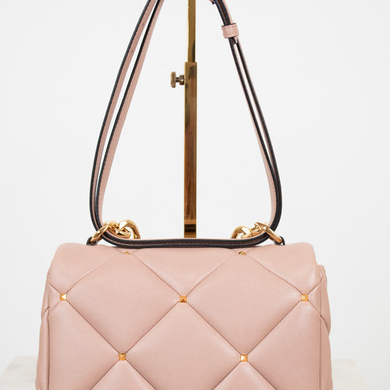 Pink quilted handbag with gold accents on a white background