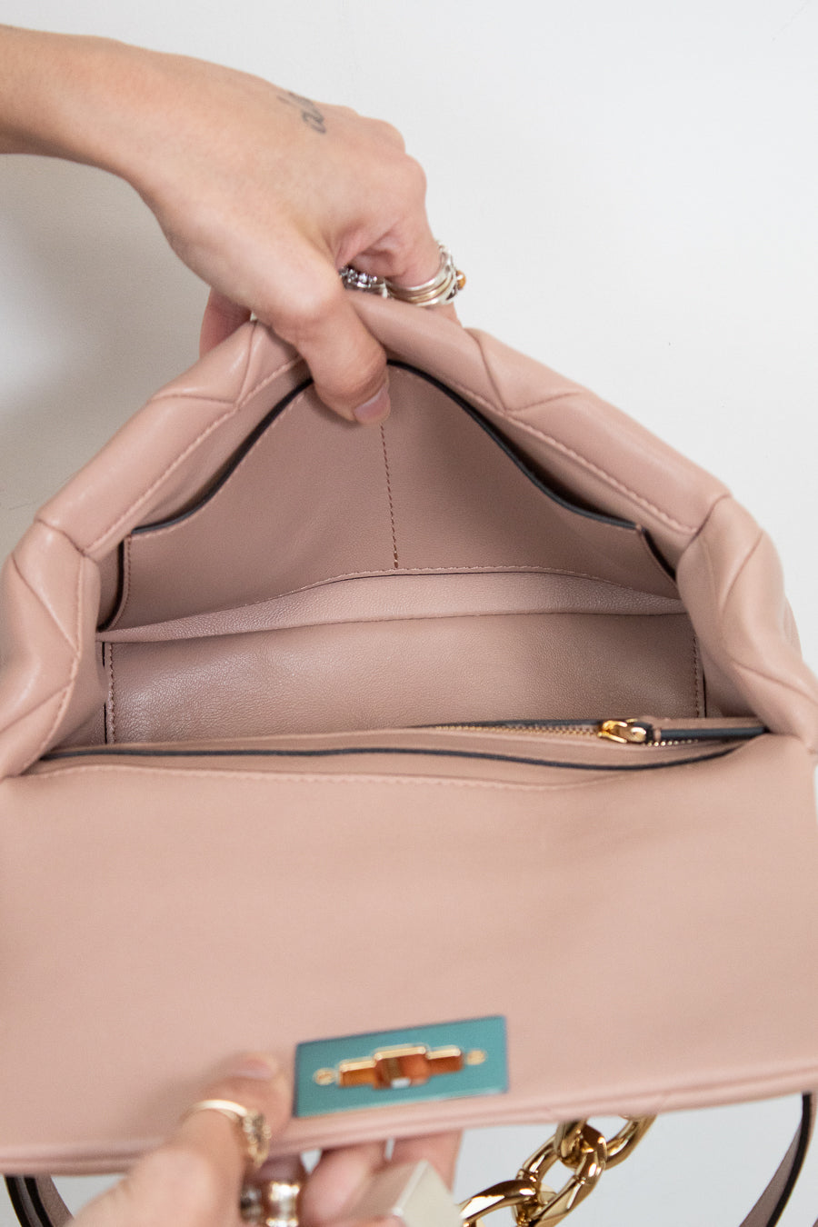 Close-up of a pink handbag with a gold zipper and visible brand logo on a white background.