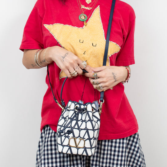 Person wearing a red shirt with a yellow star design, holding a patterned handbag against a plain background.
