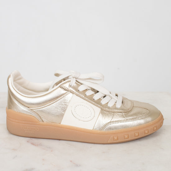Side view of cream and gold low top sneakers