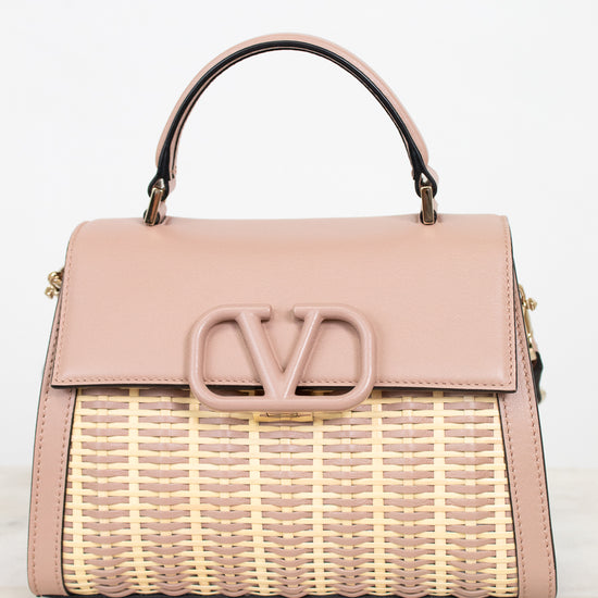 Pink handbag with wicker design and visible brand logo on a light background