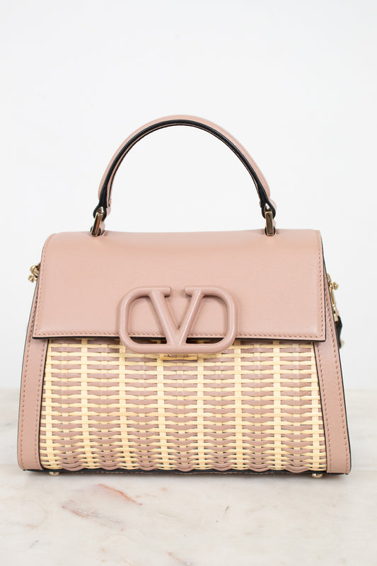 Pink handbag with wicker design and visible brand logo on a light background