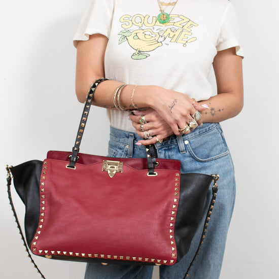 Person holding a red and black handbag against a plain background
