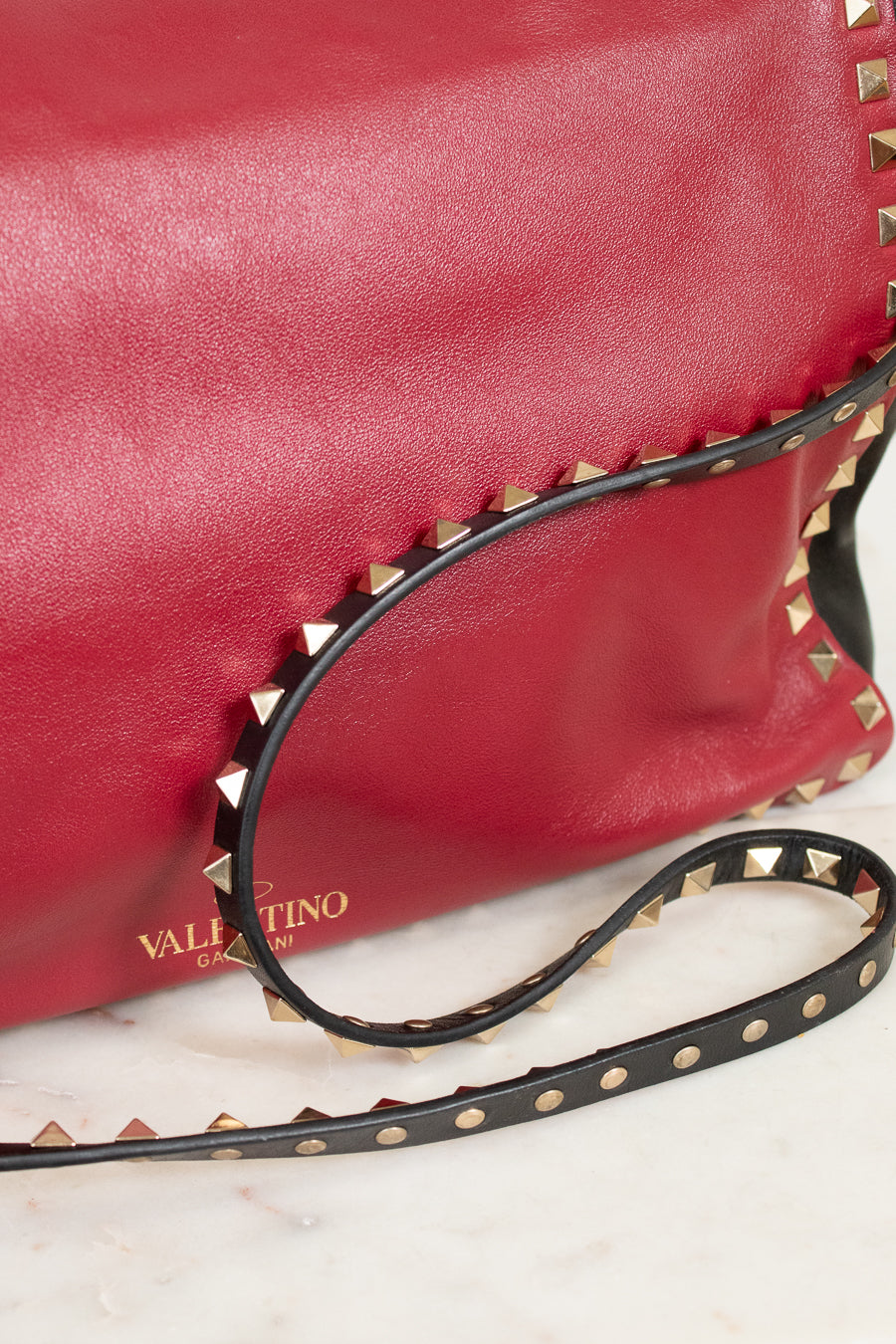 Red leather handbag with gold studs and a black strap on a light background