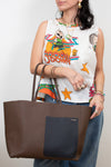Person holding a brown tote bag with a colorful sleeveless top featuring graphics.