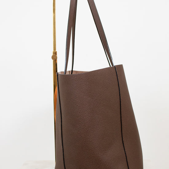 Brown leather tote bag with wooden handle on a white background