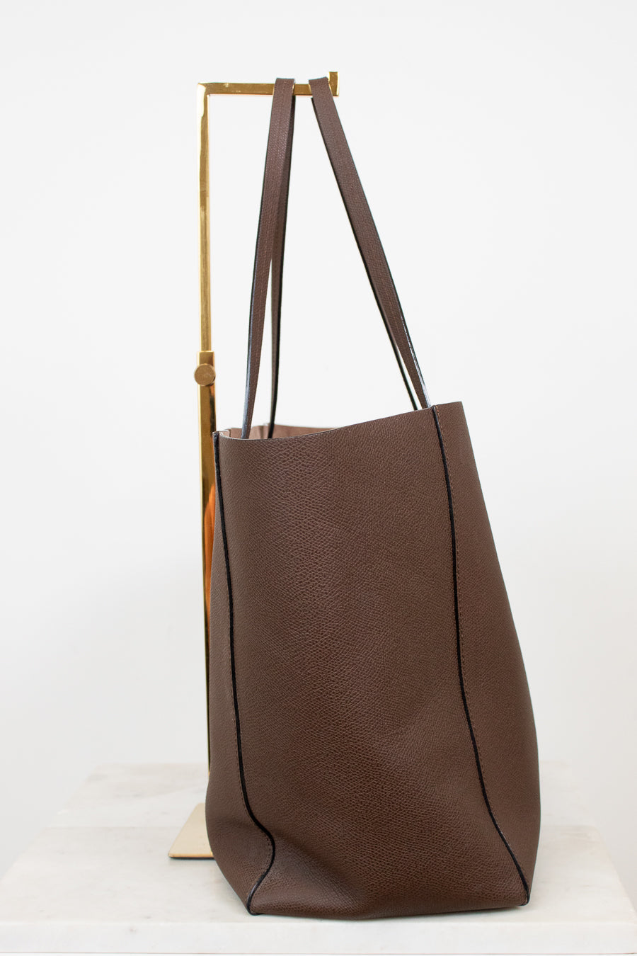 Brown leather tote bag with wooden handle on a white background