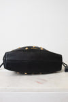A black leather bag with gold-tone studs and the brand name 'VERONICA BEARD' printed on the front, resting on a white marble surface against a white background.