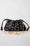 A black leather drawstring clutch bag by Veronica Beard, embellished with gold-tone studs and featuring a gold chain strap, resting on a white surface against a white background.