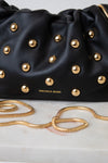 Close-up of a black leather handbag with gold studs and a gold chain strap, with the brand name 'VERONICA BEARD' printed in gold on the front.