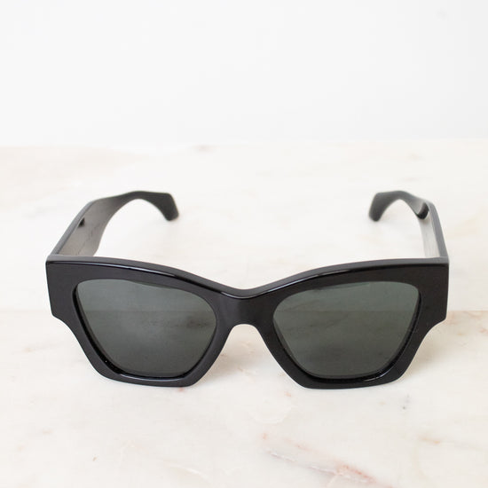 Black cat-eye sunglasses with dark tinted lenses, resting on a light marble surface against a white background.