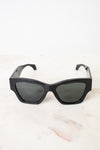 Black cat-eye sunglasses with dark tinted lenses, resting on a light marble surface against a white background.