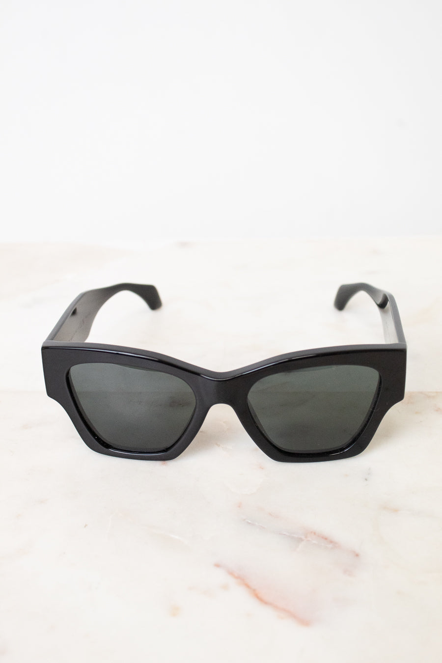 Black cat-eye sunglasses with dark tinted lenses, resting on a light marble surface against a white background.