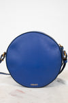 A round blue leather crossbody bag with gold-tone hardware and a small gold VERSACE logo on the back, displayed on a light marble surface against a white background.