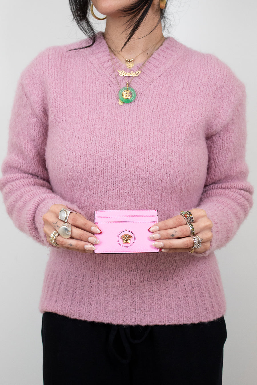 Person wearing a pink sweater holding a pink wallet against a plain background