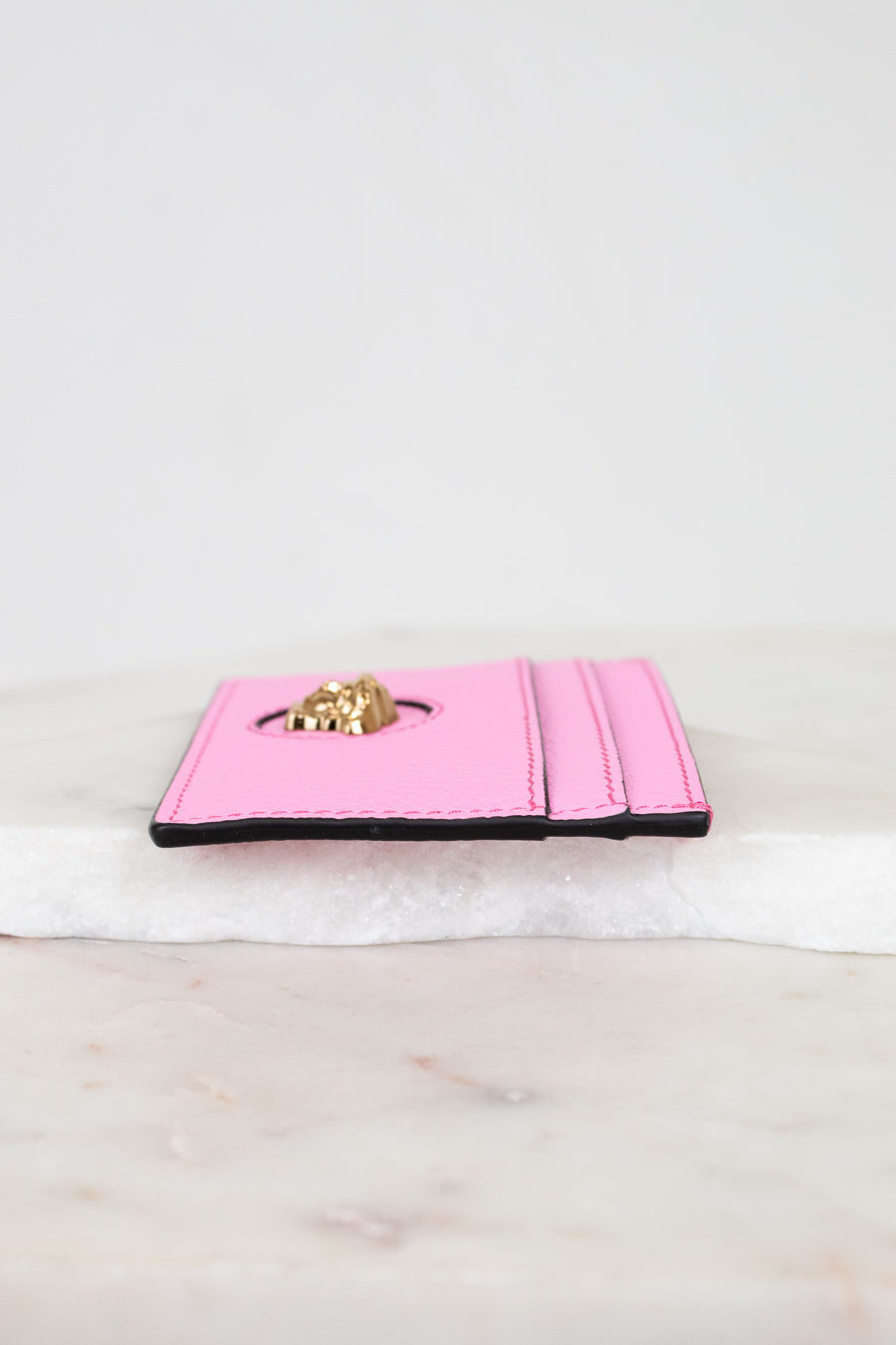 Pink wallet with gold logo on a marble surface
