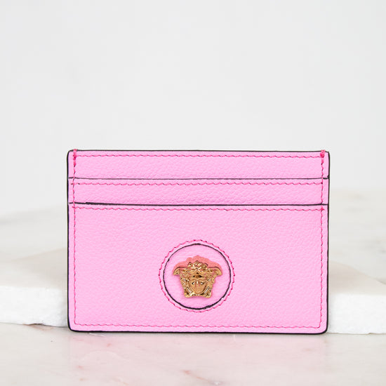 Pink cardholder with a gold logo on a marble surface