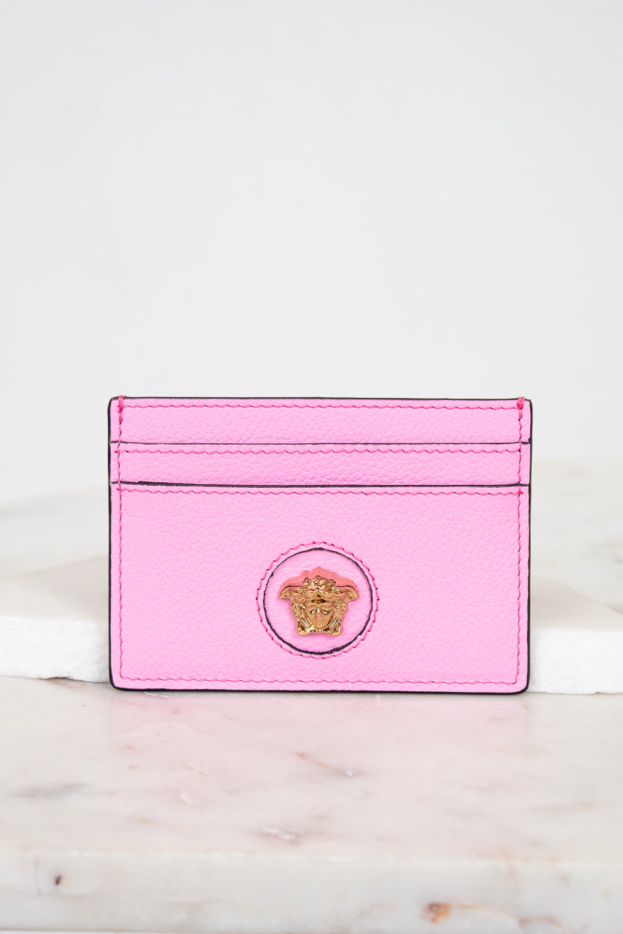 Pink cardholder with a gold logo on a marble surface