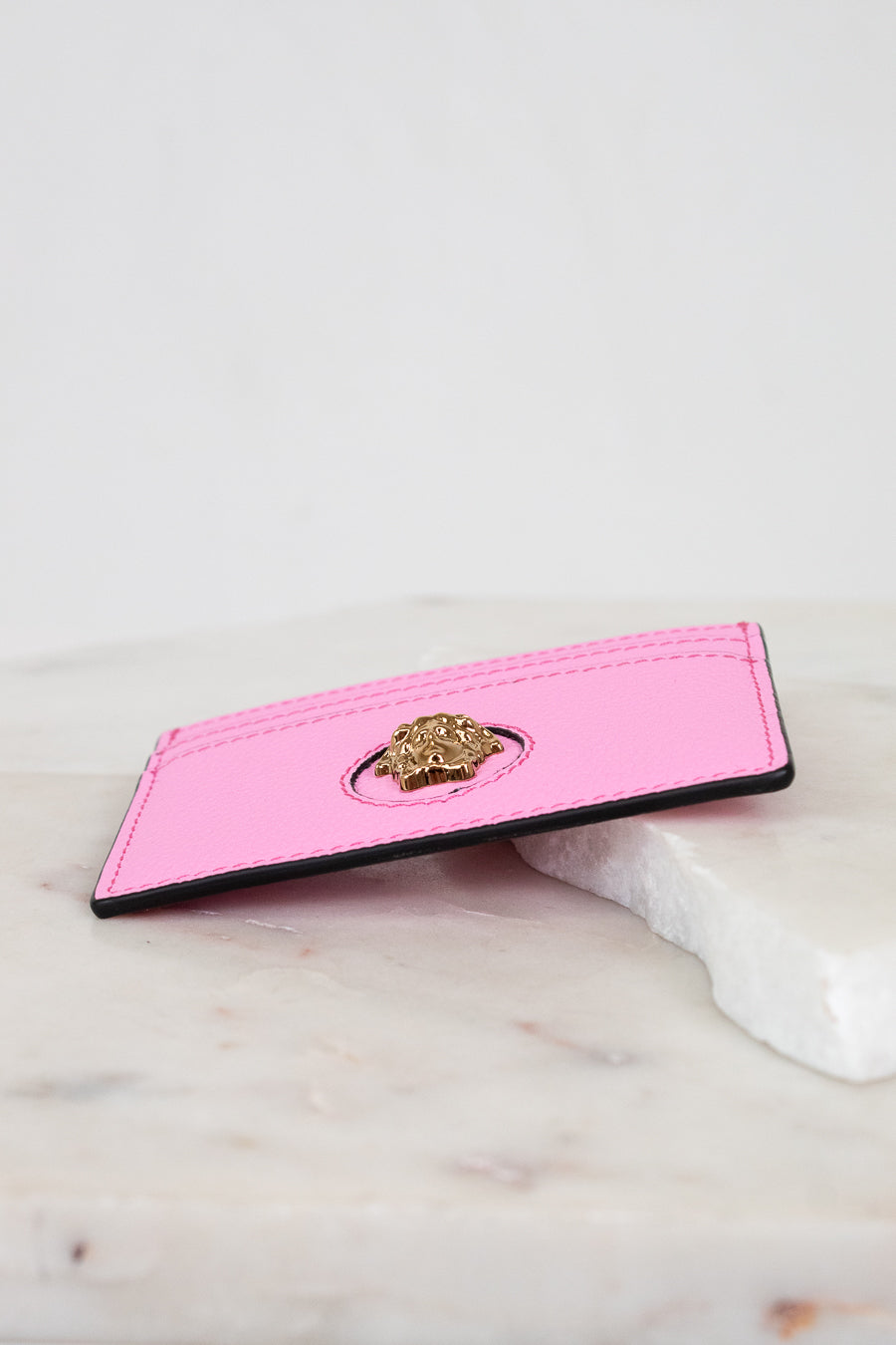 Pink cardholder with gold lion emblem on a marble surface