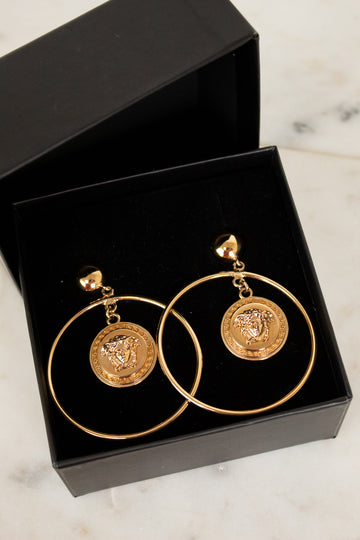 Gold hoop earrings with coin designs in a black box on a marble surface