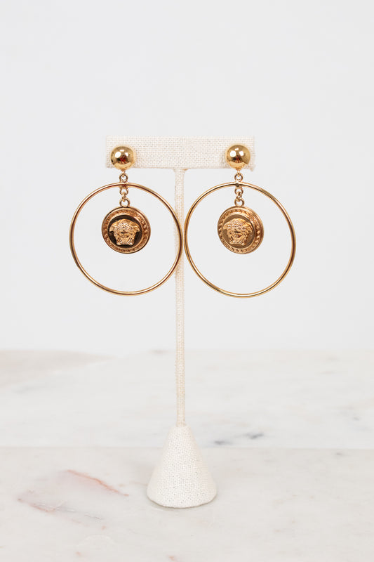 Gold hoop earrings with circular designs on a white stand against a light background