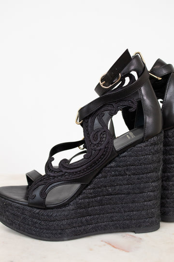 Black wedge sandals with detailed straps on a white background
