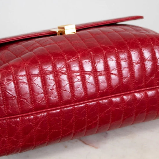 Red crocodile skin handbag with gold clasp on a light gray background