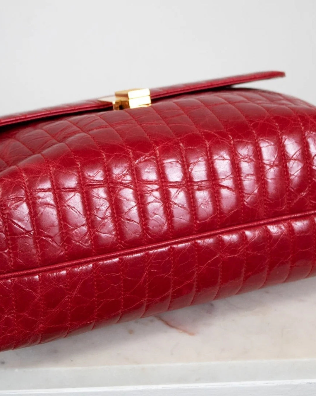 Red crocodile skin handbag with gold clasp on a light gray background