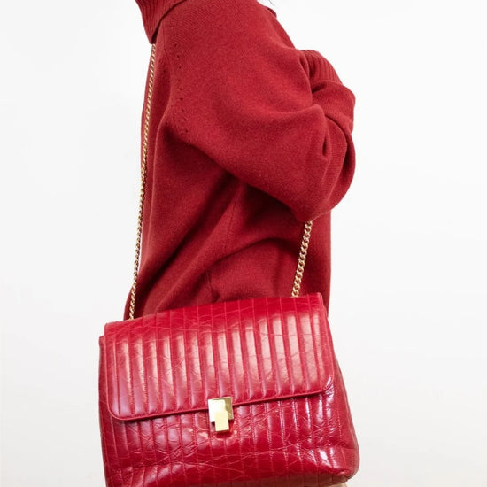 Person wearing a red crocodile-patterned handbag on a white background