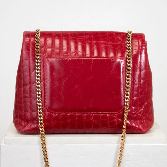 Red crocodile-patterned handbag with a gold chain on a white background