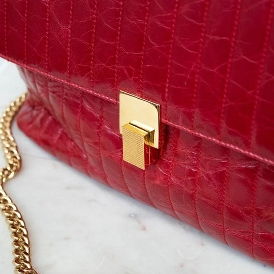 Red textured handbag with a gold chain strap on a marble surface
