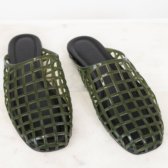 A pair of olive green open-toe mule sandals with a glossy grid pattern, displayed on a white marble surface against a white background.