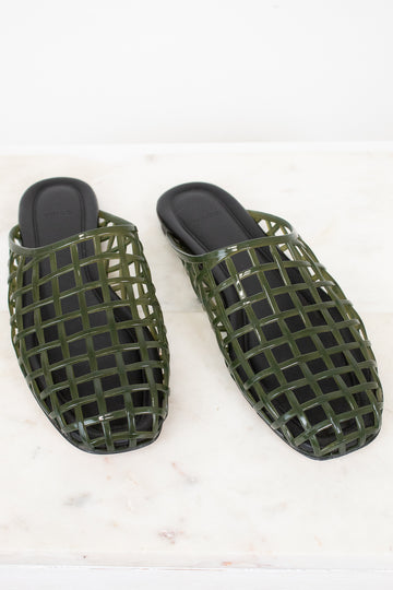A pair of olive green open-toe mule sandals with a glossy grid pattern, displayed on a white marble surface against a white background.