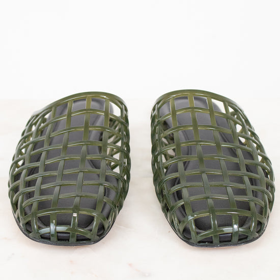 A pair of olive green plastic shoe guards or protective covers with a woven grid pattern, displayed on a light marble surface against a white background.