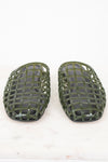 A pair of olive green plastic shoe guards or protective covers with a woven grid pattern, displayed on a light marble surface against a white background.