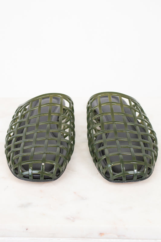 A pair of olive green plastic shoe guards or protective covers with a woven grid pattern, displayed on a light marble surface against a white background.