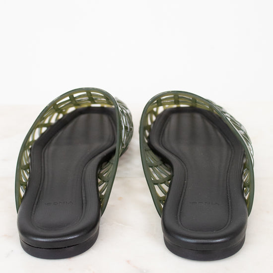 A pair of green jelly sandals with black footbeds, shown from the bottom on a white marble surface.