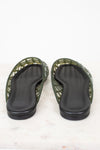 A pair of green jelly sandals with black footbeds, shown from the bottom on a white marble surface.