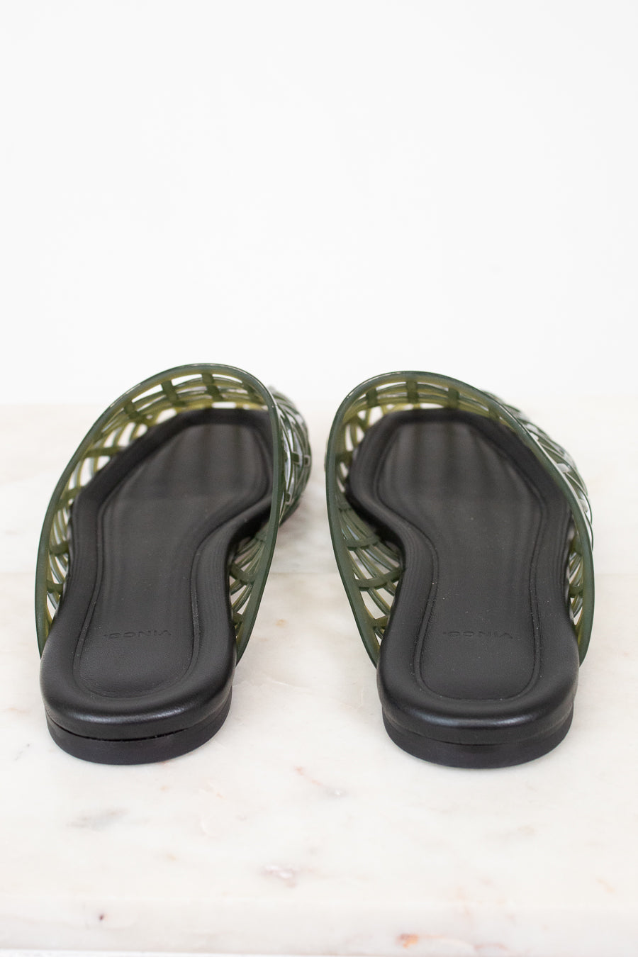 A pair of green jelly sandals with black footbeds, shown from the bottom on a white marble surface.