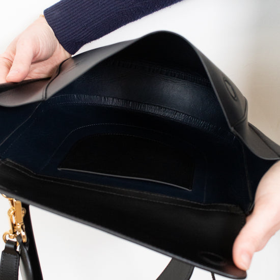 Black handbag held open by a person wearing a blue sleeve.