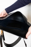 Black handbag held open by a person wearing a blue sleeve.