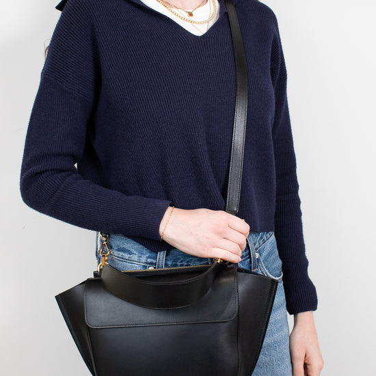 Person wearing a navy sweater and holding a black leather bag against a white background