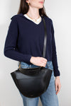 Person wearing a navy sweater and holding a black leather bag against a white background