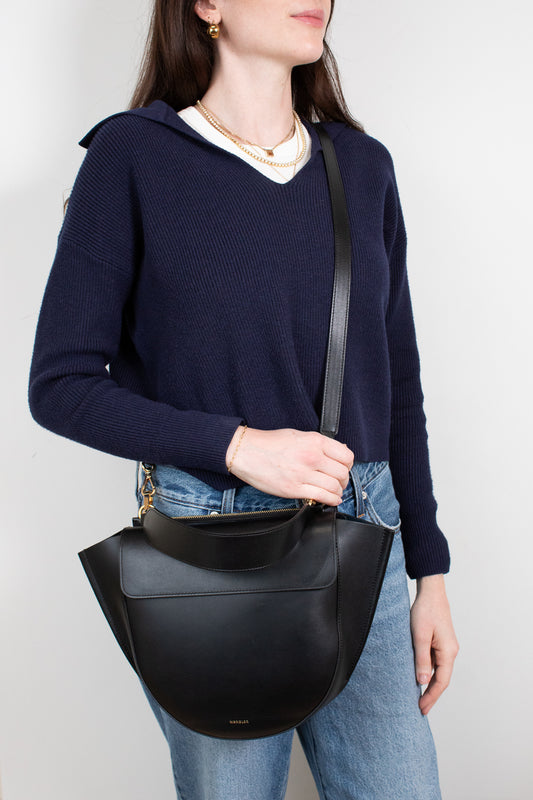 Person wearing a navy sweater and holding a black leather bag against a white background