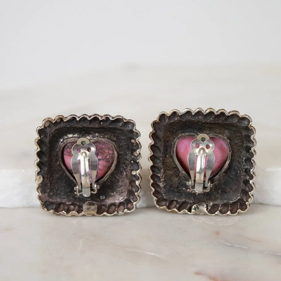 Pair of earrings with heart-shaped pink and silver accents on a marble surface.