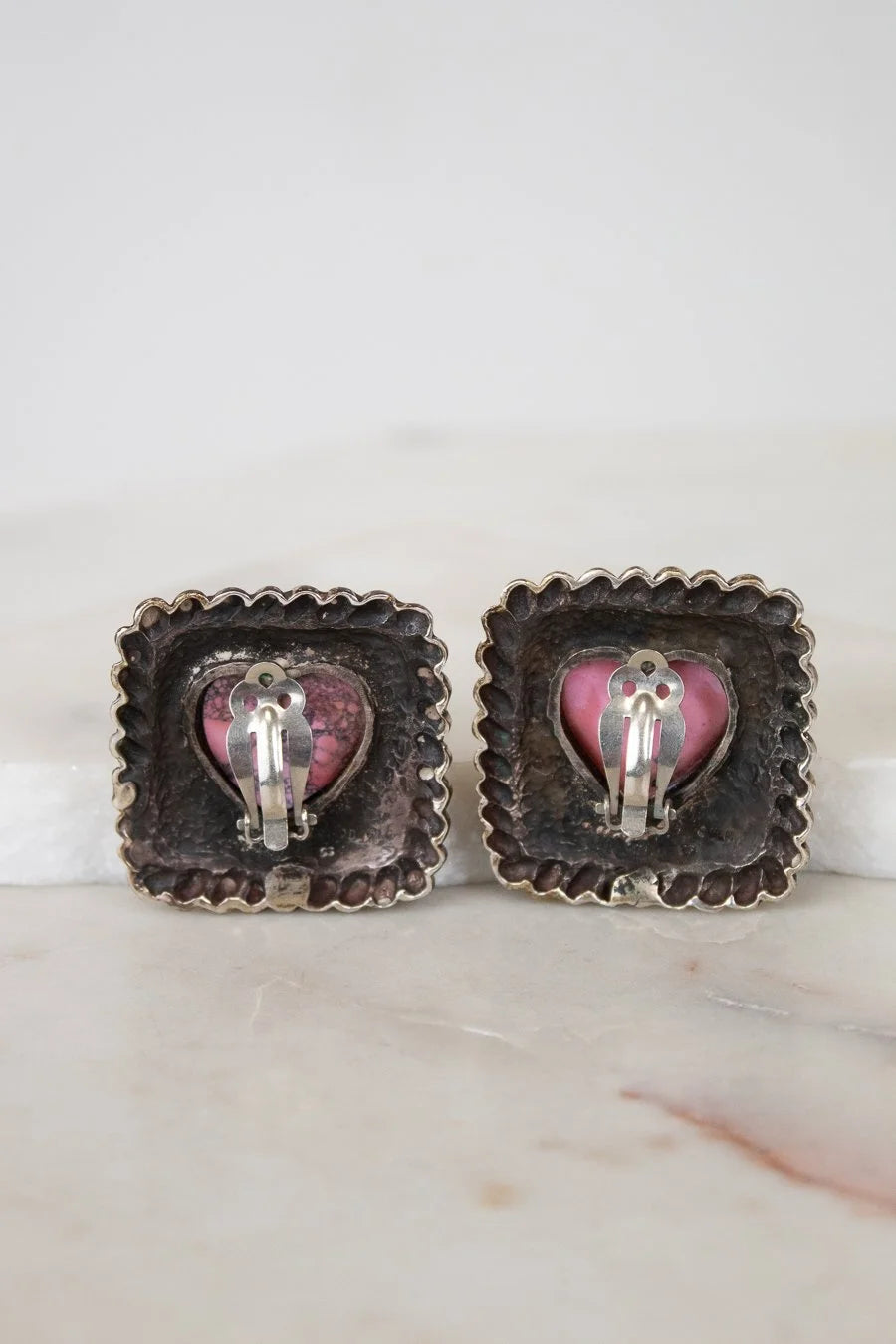 Pair of earrings with heart-shaped pink and silver accents on a marble surface.